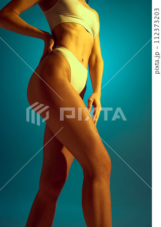 Smooth and toned legs. Cropped photo of young female legs, buttocks in yellow neon light against gradient studio background. Smooth and toned legs. Cropped photo of young female legs, buttocks in yellow neon light against gradient studio background. 112373203