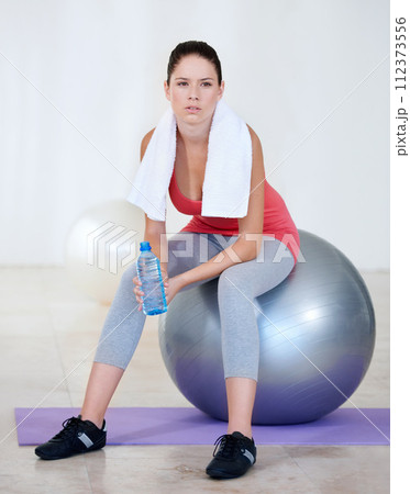Ball, relax or woman drinking water on break after exercise, workout or fitness training in gym. Thinking, tired lady or thirsty sports athlete with liquid bottle for wellness, resting or hydration 112373556