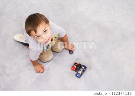Car, toys and portrait of kid playing for learning, development and fun at modern home. Cute, top view and sweet young boy child enjoying game with vehicles on floor for childhood hobby at house. 112374139