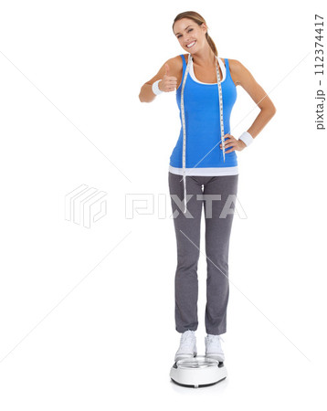 Woman thumbs up, scale and measure tape in studio for fitness, weight loss or health goals, like or yes. Portrait of model with results, progress and workout or diet feedback on a white background 112374417
