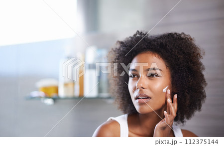 African woman, skincare and facial cream with smile, wellness or afro in home bathroom for morning routine. Girl, person and serum with cosmetics, beauty or transformation with self care in apartment 112375144