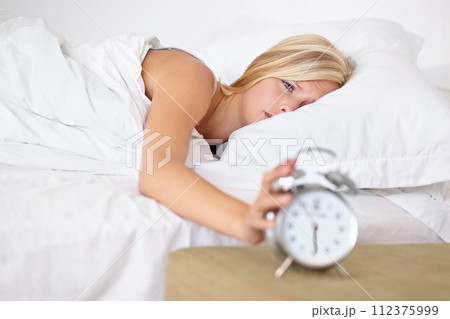Tired, woman and wake up with alarm in morning and sleeping on bed in home with stress or fatigue. Press, snooze and girl frustrated with clock and time to start day in bedroom and apartment 112375999