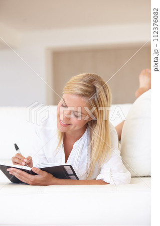Writing, notebook and planning with woman on sofa for goals, diary and schedule. Calendar, relax and list with female person and journal in living room of home for self care, reflection and idea 112376082