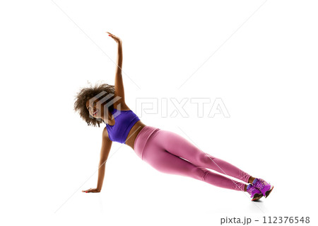 Athletic African-American woman in purple activewear balancing, training against white studio background. Athletic African-American woman in purple activewear balancing, training against white studio background. 112376548