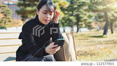 Happy asian woman, phone and sitting on park bench for social media, communication or networking. Female person smile in relax on mobile smartphone for online search, streaming or reading in nature 112377953
