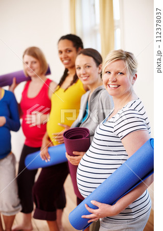 Keeping active during pregnancy. A multi-ethnic group of pregnant women holding their exercise mats in a gym. 112378037