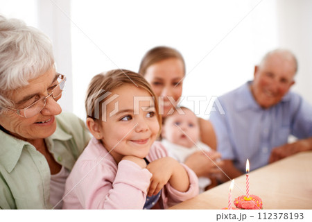 Family, birthday party and cupcake with candle for celebration, mother and grandparents with children at home. Happy young girl with cake, people and smile for anniversary with dessert at event 112378193