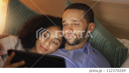 Couple, smile and relax in bedroom with tablet at night, streaming movie or film. Happy, technology and man and woman in bed on social media, browsing online app and watching video together in home 112378284