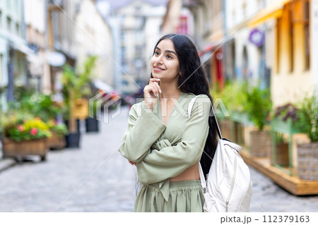 Indian young beautiful woman standing outside on a city street, posing with a hand to her face and looking to the side smiling. Indian young beautiful woman standing outside on a city street, posing with a hand to her face and looking to the side smiling. 112379163