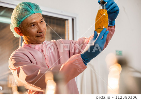 A colleague in a beverage factory inspects Basil seed products on the conveyor belt. His dedication as an inspector contributes to maintaining the industry's high manufacturing and quality standards. A colleague in a beverage factory inspects Basil seed products on the conveyor belt. His dedication as an inspector contributes to maintaining the industry's high manufacturing and quality standards. 112380306