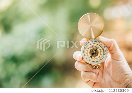 With the backdrop of a serene forest and tranquil lake a woman's hand firmly grasps a compass symbolizing guidance and the exciting spirit of exploration. 112380309