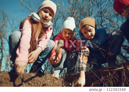 Little explorers in casual attire engaging with natural world, investigating dirt. Environment lesson. Outdoor activities for children's development. 112381589