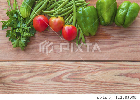 Frame of red tomatoes, green bell peppers, cucumber, green beans and parsley on a wooden background Frame of red tomatoes, green bell peppers, cucumber, green beans and parsley on a wooden background 112383989