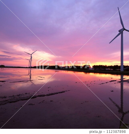 夕焼けに染まる水を張った田んぼと風車 夕焼けに染まる水を張った田んぼと風車 112387898