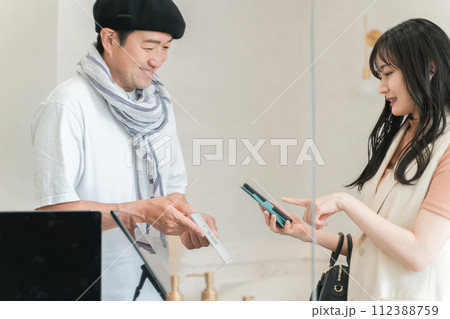 スマホでQRコード決済・スマホ決済・バーコード決済・オンライン決済・電子決済で会計する女性客 112388759