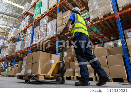Man African American worker wear safety uniform push load cart product to shelf in warehouse store. Man African American worker wear safety uniform push load cart product to shelf in warehouse store. 112389521