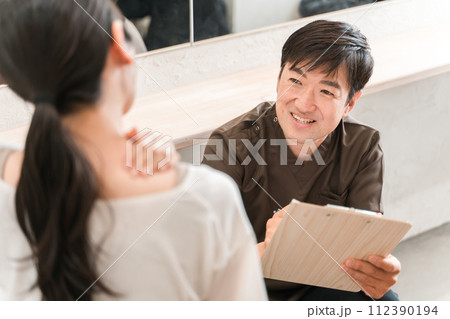 整体院・整骨院でカウンセリング・診察・相談・問診する整体師・セラピストの男性と女性客（肩こり） 112390194