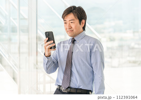 待ち合わせでスマホを見る中年のアジア人男性ビジネスマン 112391064