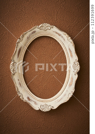茶色い壁紙に掛けられたアンティークな楕円形の額縁 112391699