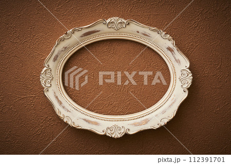 茶色い壁紙に掛けられたアンティークな楕円形の額縁 112391701
