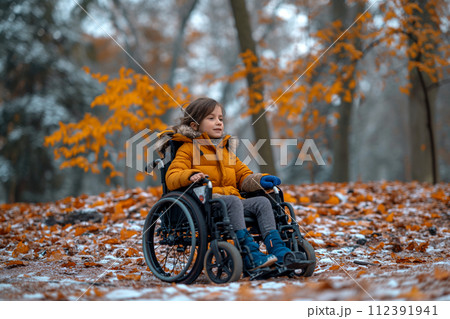 A girl sits on a wheelchair in a park in winter 112391941