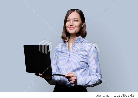 Smiling young business woman with laptop on grey background Smiling young business woman with laptop on grey background 112396543