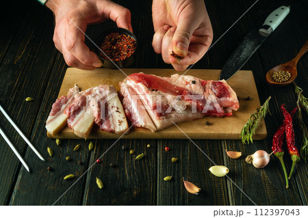 The process of preparing sandwiches for snacks from lard and seasonings in the pub kitchen. Chef hands add dry spices to pork lard with a knife on a wooden cutting board The process of preparing sandwiches for snacks from lard and seasonings in the pub kitchen. Chef hands add dry spices to pork lard with a knife on a wooden cutting board 112397043