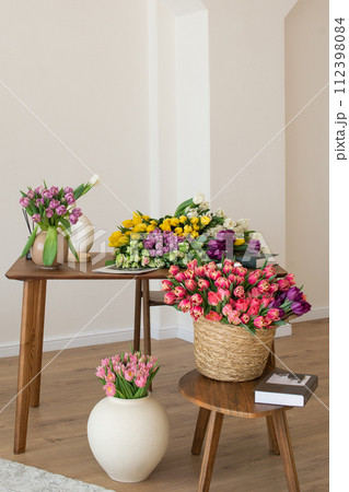 Variety of tulips in baskets and vases on wooden tables. 112398084