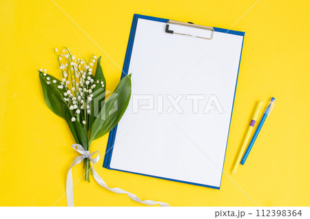 A blue folder as a template with a place to copy on a yellow table with lilies of the valley 112398364