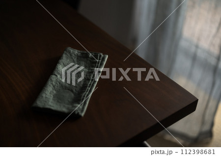 Dark green linen napkin on walnut table indoor with natural window light 112398681