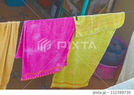 Colorful clothes after washing are hung on a clothesline to dry in the wind, pink, yellow towels. Household hygiene items 112398730