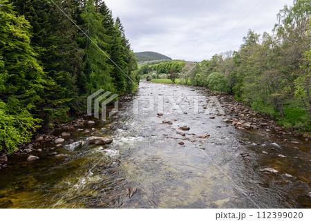 Serene river meanders through vibrant green Scottish forests, with hills on the horizon Serene river meanders through vibrant green Scottish forests, with hills on the horizon 112399020