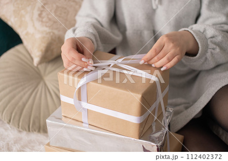 Person tying a white ribbon on brown paper gift boxes. 112402372
