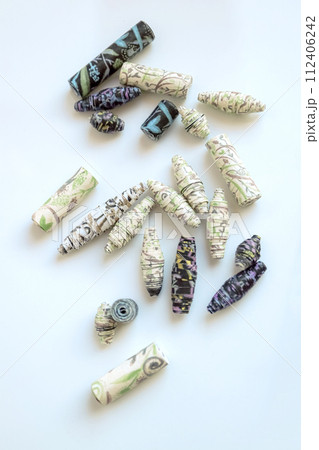 Handmade paper beads of brown, green, black colored floral patterns lying on white table Handmade paper beads of brown, green, black colored floral patterns lying on white table 112406242