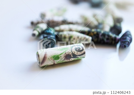 Handmade paper beads of brown, green, black colored floral patterns lying on white table side view 112406243