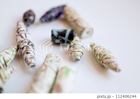 Handmade paper beads of brown, green, black colored floral patterns lying on white table side view Handmade paper beads of brown, green, black colored floral patterns lying on white table side view 112406244