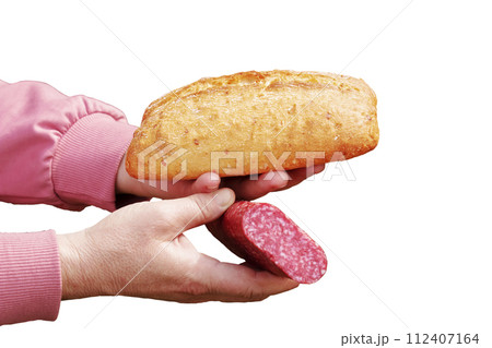 Bread and sausage in the hand of a middle-aged woman. The concept of the world food crisis associated with the war in Ukraine. Isolated on white background Bread and sausage in the hand of a middle-aged woman. The concept of the world food crisis associated with the war in Ukraine. Isolated on white background 112407164