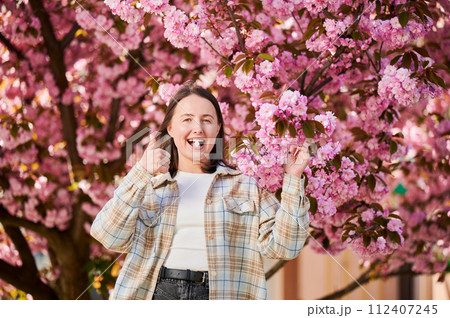 Woman allergic suffering from seasonal allergy at spring. Young happy woman applying allergy pill, giving thumbs up, posing in blossoming garden at springtime. Antihistamine medication concept 112407245