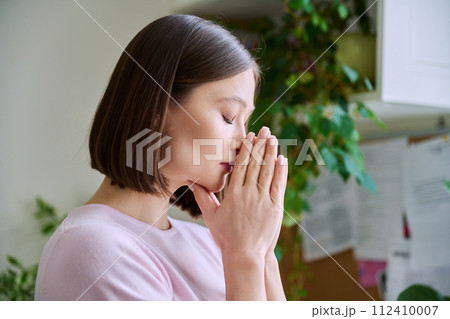 Profile view close-up of young woman's face with hands folded in prayer, dreams 112410007