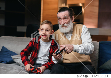 Cute little boy with grandfather sitting on sofa and playing video game with game pad 112410951