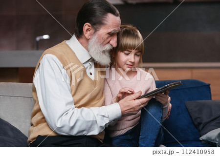 Little girl teach grandpa to use modern smart devices. Communication of young and senior generation. Enjoy leisure time with family. 112410958