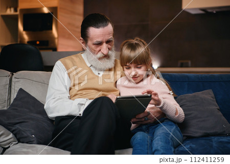 Grandfather with his granddaughter using tablet at home 112411259