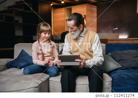 Grandpa with his granddaughter using tablet at cozy home. Grandpa with his granddaughter using tablet at cozy home. 112411274