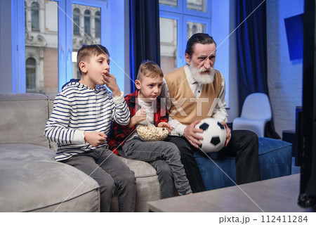 Likable concentrated senior bearded grandfather with his cheerful 10-15s grandsons spending their free time at revision the basketball game on tv 112411284