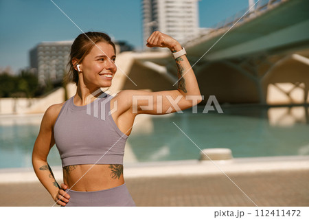 Female model in sportswear showing biceps standing outdoors and looks away 112411472