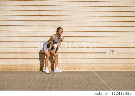 Smiling woman in sportswear have a rest after workout outside standing on wall background 112411489