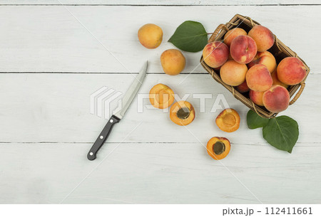 Ripe apricots and apricot leaves in a bowl on a wooden table. Fresh fruits from the home garden Ripe apricots and apricot leaves in a bowl on a wooden table. Fresh fruits from the home garden 112411661