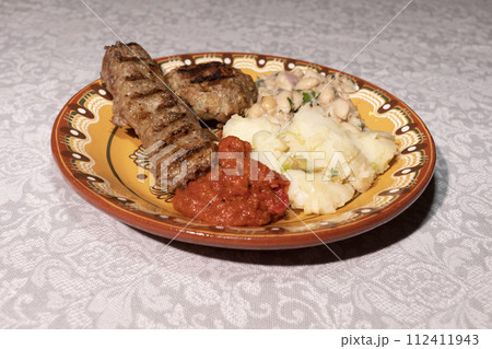 Plate With Traditional Bulgarian Food. Mashed Potato, Vegetable Relish Ljutenica, White Beans, Haricot, Grilled Minced Meat With Spices Kebapche. Horizontal Plane. 112411943