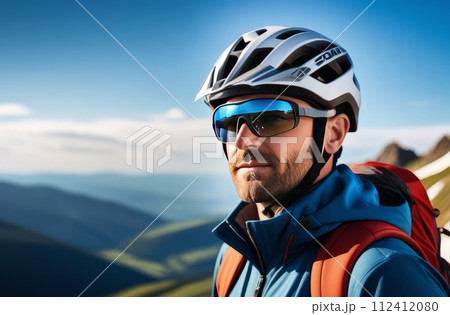 Man wearing helmet and sunglasses glasses stands confidently before towering mountain backdrop ready for adventure, exploration. He may be gearing up for bicycle ride, some other outdoor activity. 112412080
