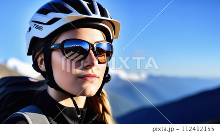 Woman wearing helmet and sunglasses glasses stands confidently before towering mountain backdrop ready for adventure, exploration.She may be gearing up for bicycle ride or some other outdoor activity. 112412155